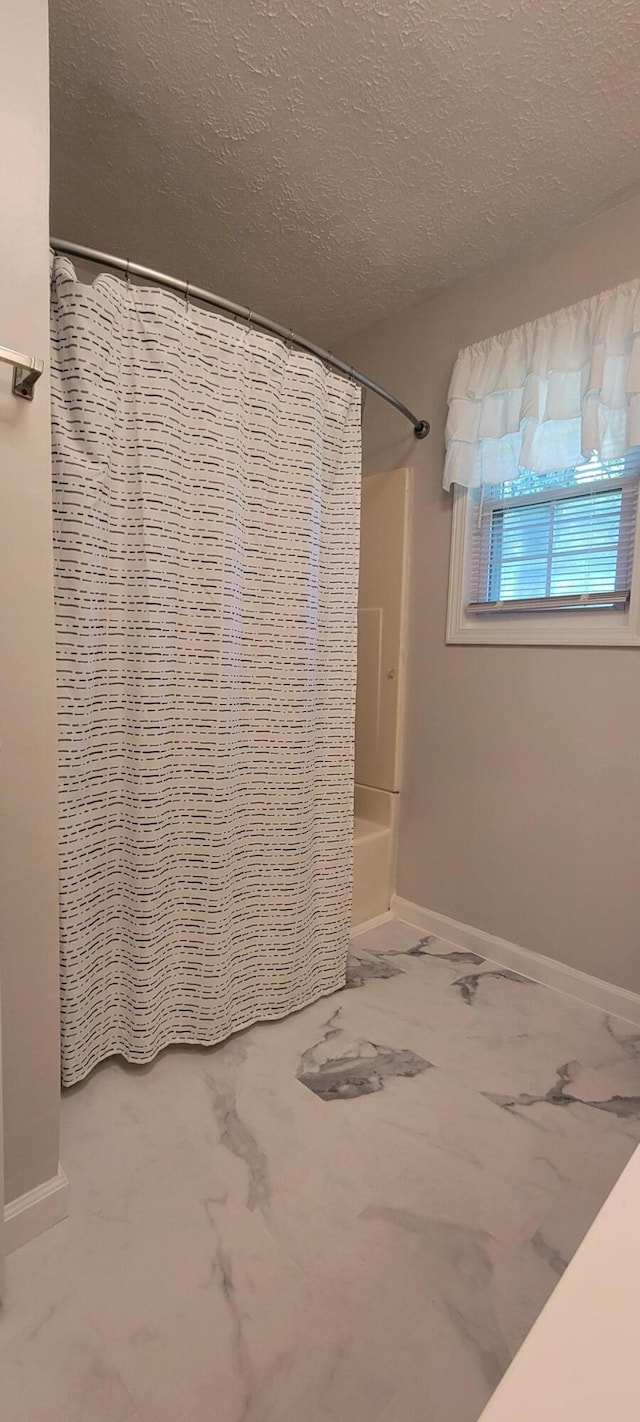 bathroom with marble finish floor, a textured ceiling, baseboards, and shower / bath combination with curtain