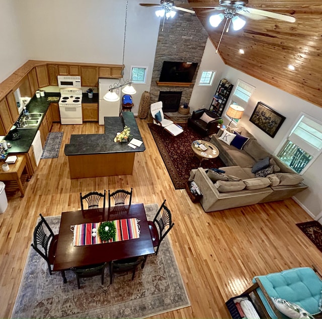 living room with high vaulted ceiling, light hardwood / wood-style floors, ceiling fan, and a stone fireplace