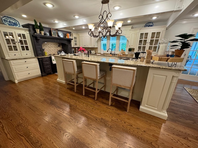 kitchen with decorative backsplash, a spacious island, a kitchen bar, light stone counters, and dark hardwood / wood-style flooring