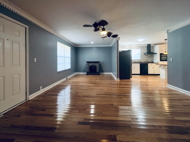 unfurnished living room featuring ornamental molding, wood-type flooring, ceiling fan, and a wood stove