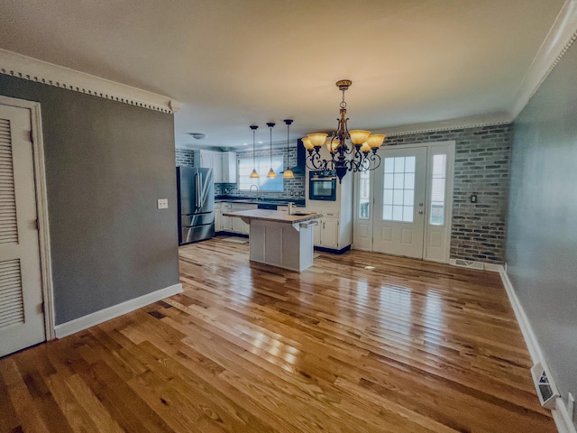 unfurnished dining area featuring brick wall, crown molding, a notable chandelier, and light wood-type flooring