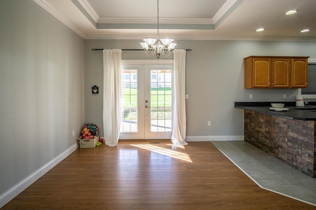 entryway with french doors, ornamental molding, a raised ceiling, hardwood / wood-style flooring, and a chandelier