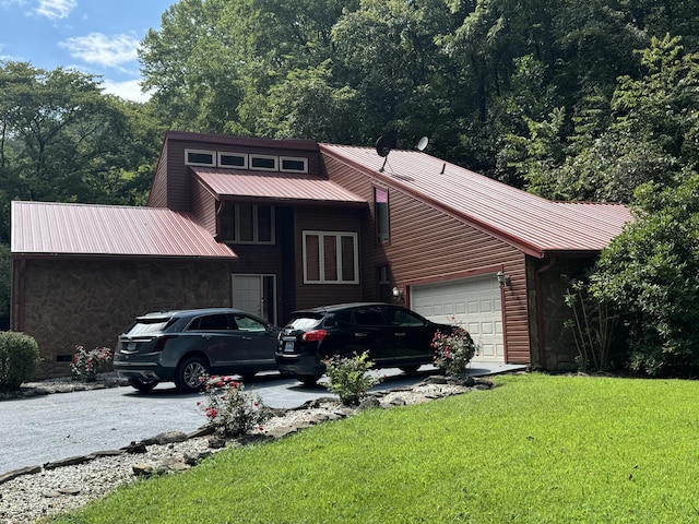 view of front of home featuring driveway, a garage, stone siding, metal roof, and a front yard