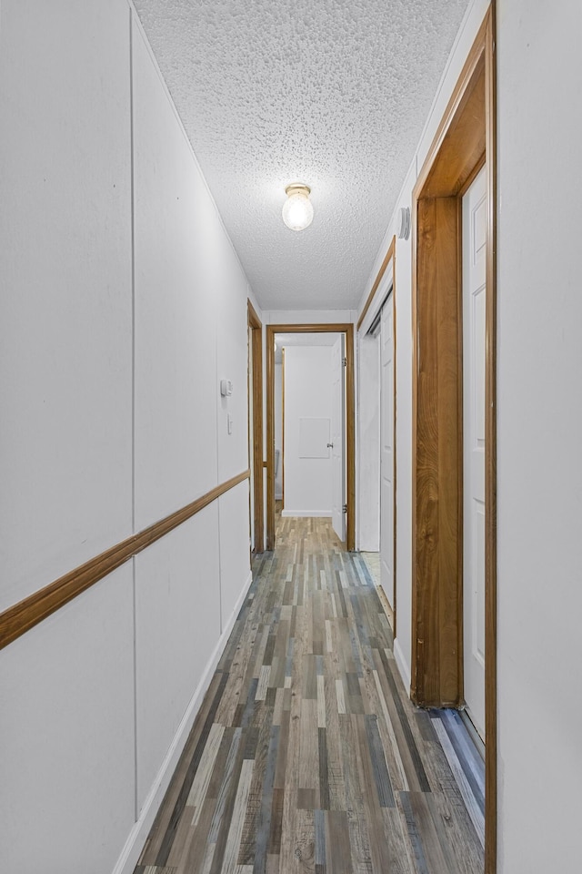 corridor with a textured ceiling and wood finished floors