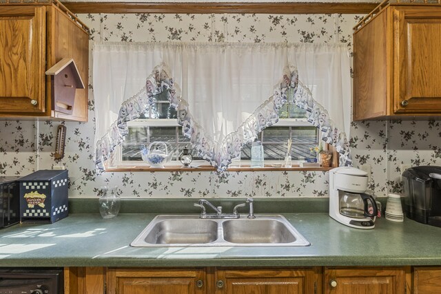 kitchen featuring brown cabinetry, a sink, and wallpapered walls