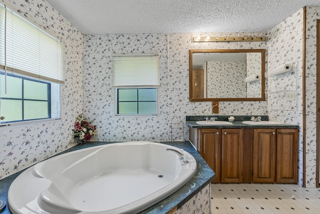 full bath featuring a textured ceiling, a garden tub, a sink, double vanity, and wallpapered walls