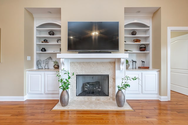 unfurnished living room with light wood-type flooring, built in shelves, and a fireplace