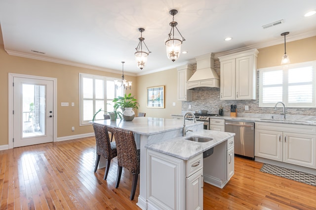 kitchen featuring decorative light fixtures, a kitchen island with sink, stainless steel dishwasher, sink, and custom exhaust hood