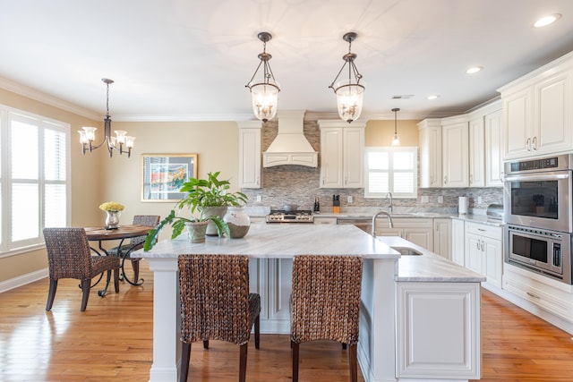 kitchen featuring a healthy amount of sunlight, an inviting chandelier, custom exhaust hood, and a center island with sink