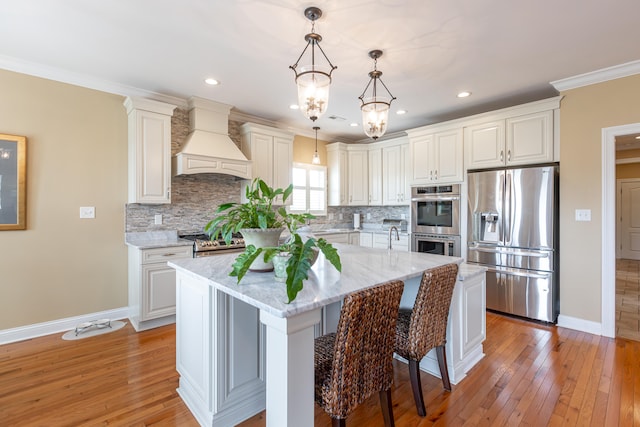 kitchen featuring a kitchen island, light stone countertops, light hardwood / wood-style floors, stainless steel appliances, and custom exhaust hood