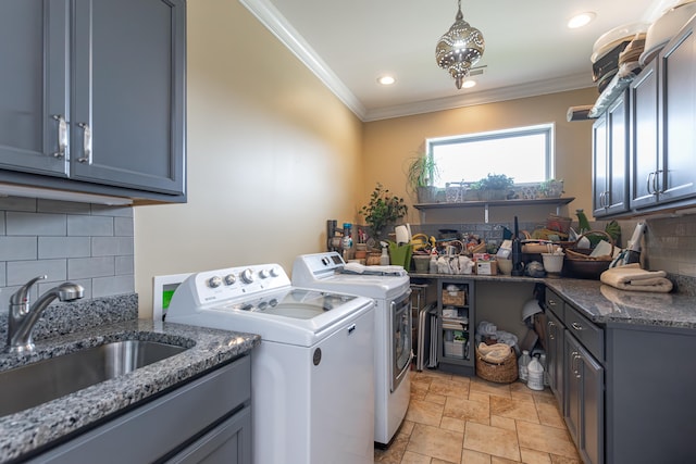 clothes washing area with ornamental molding, cabinets, washing machine and dryer, and sink