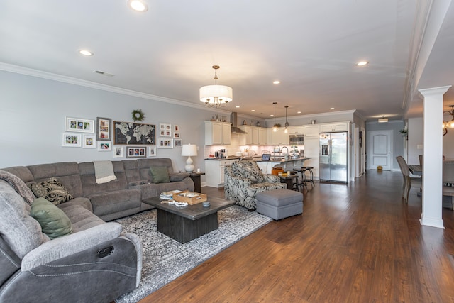 living room with dark wood-type flooring, ornamental molding, a chandelier, and ornate columns