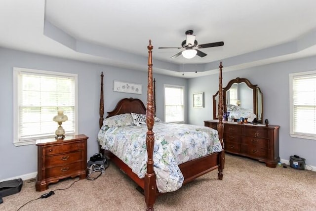 bedroom with a raised ceiling, light colored carpet, ceiling fan, and baseboards