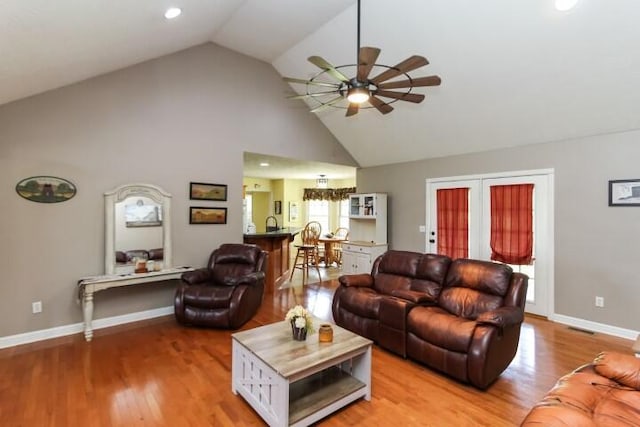 living area featuring baseboards, high vaulted ceiling, a ceiling fan, and light wood-style floors