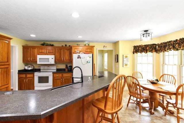 kitchen featuring dark countertops, white appliances, brown cabinets, and recessed lighting