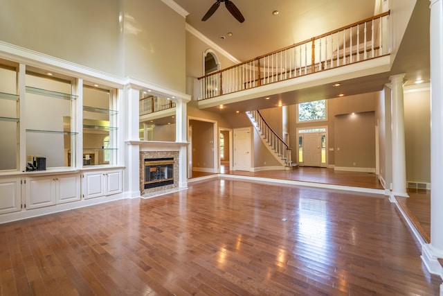 unfurnished living room featuring a towering ceiling, crown molding, ceiling fan, hardwood / wood-style flooring, and decorative columns