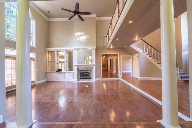 unfurnished living room featuring a fireplace, crown molding, ceiling fan, decorative columns, and hardwood / wood-style floors