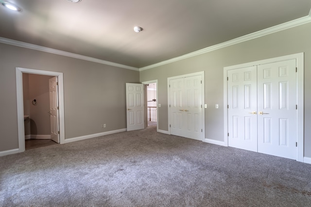 unfurnished bedroom featuring carpet, ornamental molding, ensuite bathroom, and multiple closets