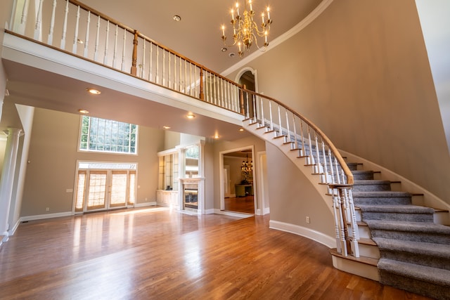 stairs featuring a towering ceiling, a fireplace, an inviting chandelier, ornamental molding, and hardwood / wood-style floors