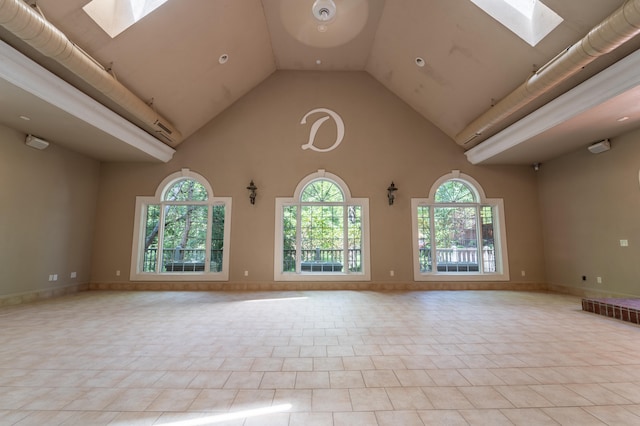 tiled spare room featuring a skylight and high vaulted ceiling