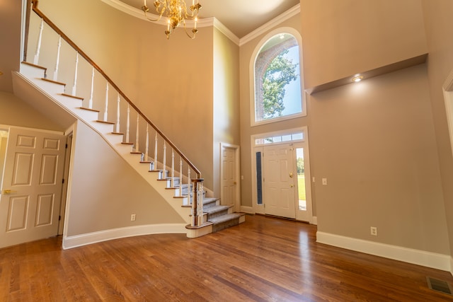 entryway featuring wood-type flooring, ornamental molding, a towering ceiling, and a chandelier