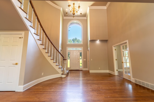 foyer entrance with a towering ceiling, an inviting chandelier, dark hardwood / wood-style floors, and ornamental molding