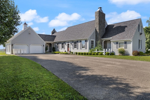 cape cod-style house featuring driveway, a chimney, roof with shingles, an attached garage, and a front lawn