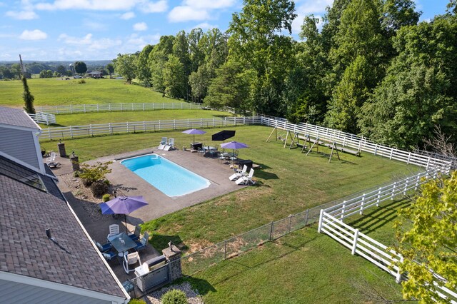 view of pool with a yard, a patio area, a rural view, and fence