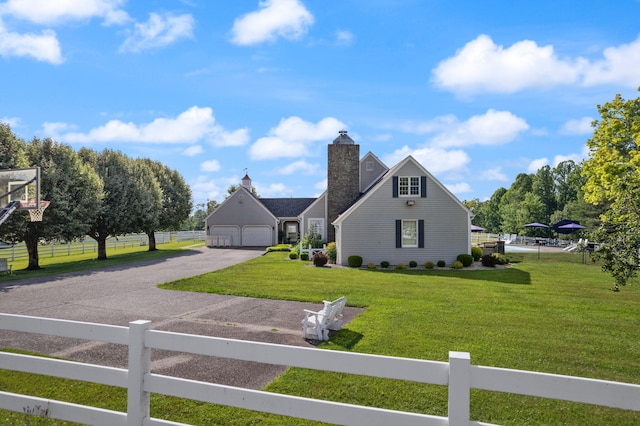 view of front of home with driveway, a chimney, an attached garage, fence, and a front yard