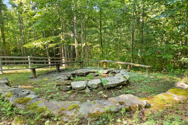 view of yard featuring a fire pit, fence, and a view of trees