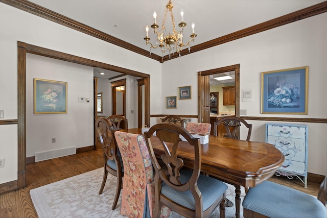 dining space with baseboards, visible vents, ornamental molding, wood finished floors, and a notable chandelier