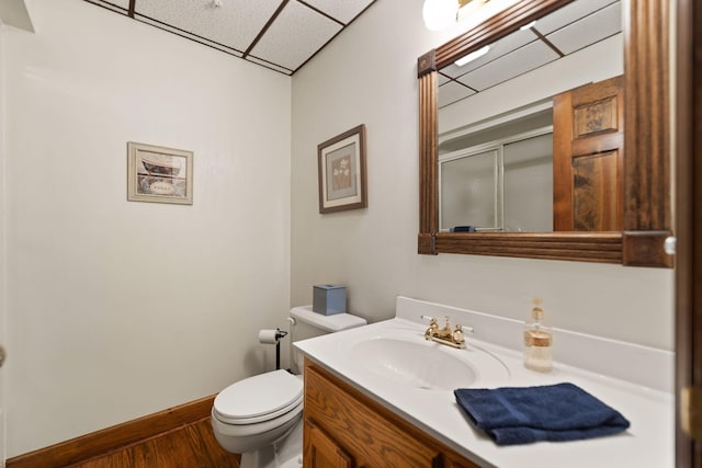 bathroom with a drop ceiling, toilet, wood finished floors, vanity, and an enclosed shower