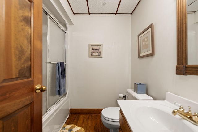 full bathroom featuring a drop ceiling, hardwood / wood-style floors, bath / shower combo with glass door, toilet, and vanity