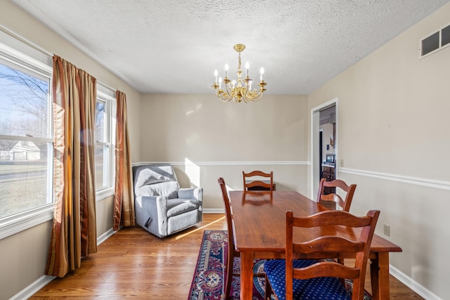 dining space featuring an inviting chandelier, a healthy amount of sunlight, a textured ceiling, and light wood-type flooring