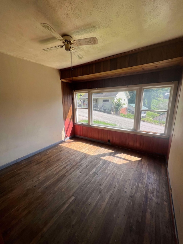 unfurnished room with ceiling fan, wooden walls, a textured ceiling, and wood-type flooring