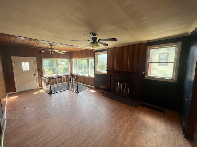 unfurnished living room featuring wood walls, ceiling fan, and wood-type flooring