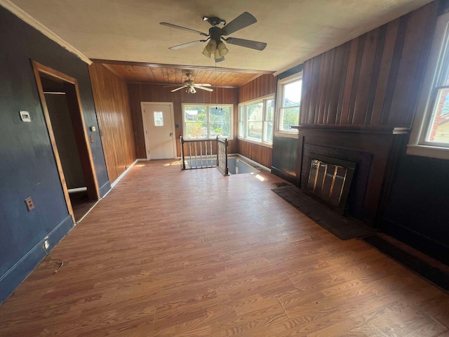unfurnished living room with a large fireplace, ceiling fan, hardwood / wood-style floors, and wood walls