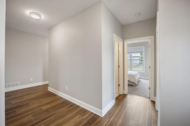 corridor with dark wood-style flooring, visible vents, and baseboards