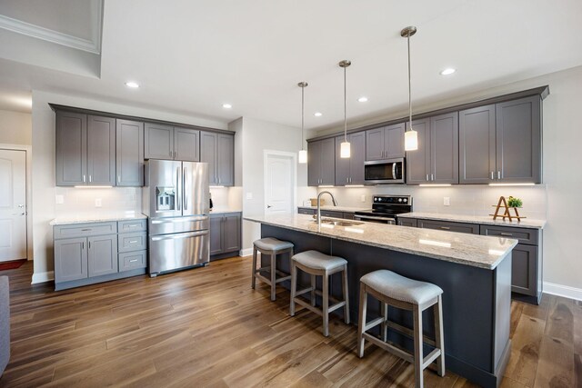 kitchen with appliances with stainless steel finishes, pendant lighting, tasteful backsplash, an island with sink, and sink