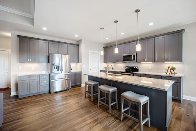 kitchen featuring pendant lighting, stainless steel appliances, a sink, an island with sink, and a kitchen bar