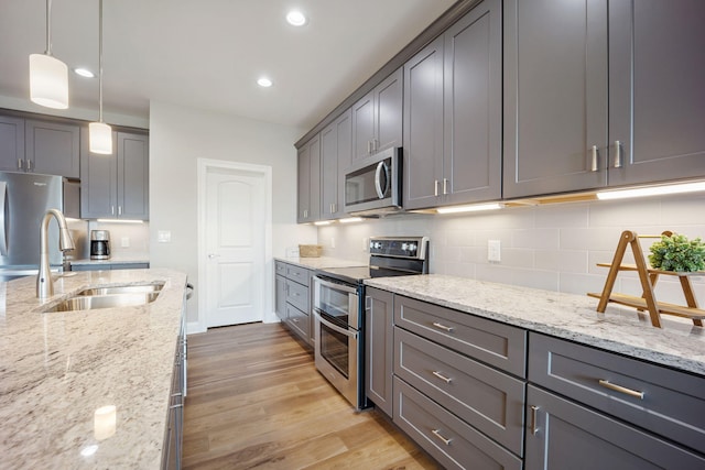 kitchen with stainless steel appliances, light stone counters, a sink, and decorative light fixtures