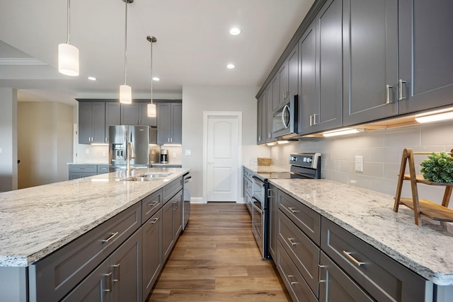 kitchen featuring a center island with sink, light stone counters, hanging light fixtures, stainless steel appliances, and a sink