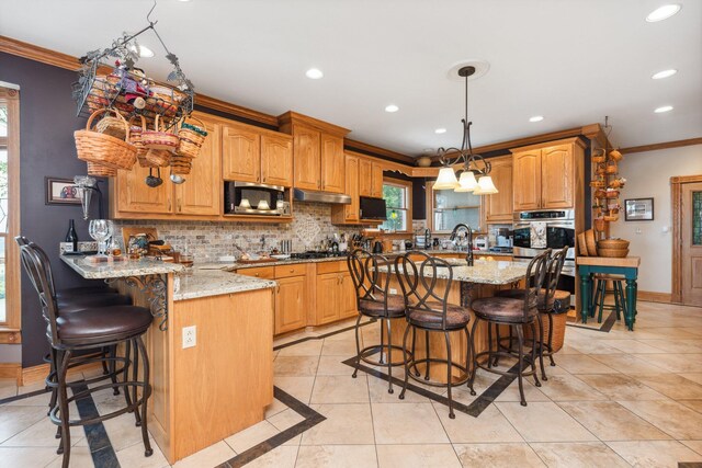 kitchen with a breakfast bar area, decorative light fixtures, appliances with stainless steel finishes, a kitchen island with sink, and light stone counters