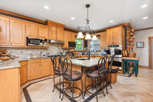 kitchen with light stone countertops, appliances with stainless steel finishes, pendant lighting, and a kitchen island with sink