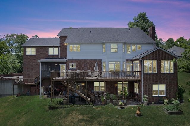 back house at dusk featuring a wooden deck and a lawn