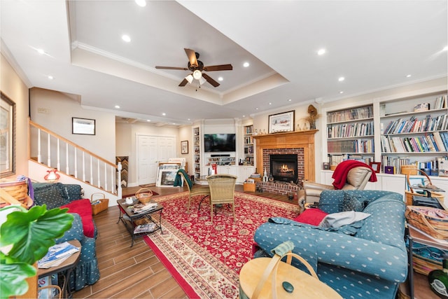 living room featuring a fireplace, crown molding, hardwood / wood-style floors, a tray ceiling, and ceiling fan