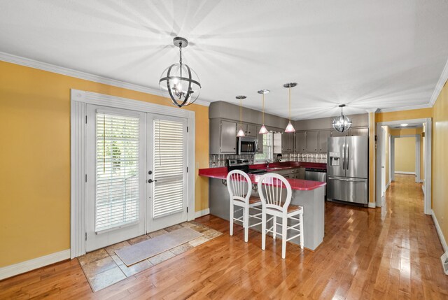 kitchen with kitchen peninsula, appliances with stainless steel finishes, backsplash, pendant lighting, and hardwood / wood-style flooring