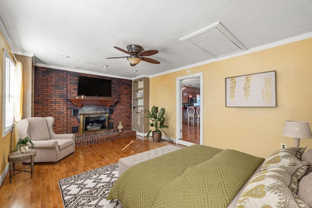 bedroom with hardwood / wood-style floors, a brick fireplace, ceiling fan, and crown molding