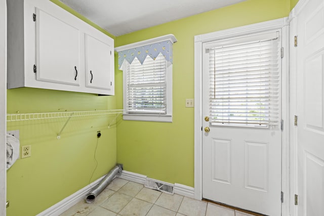 clothes washing area with electric dryer hookup, plenty of natural light, light tile patterned floors, and cabinets