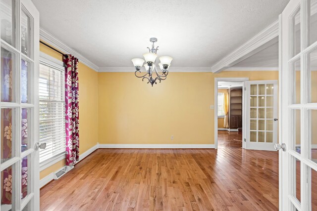 empty room with plenty of natural light, an inviting chandelier, wood-type flooring, and french doors